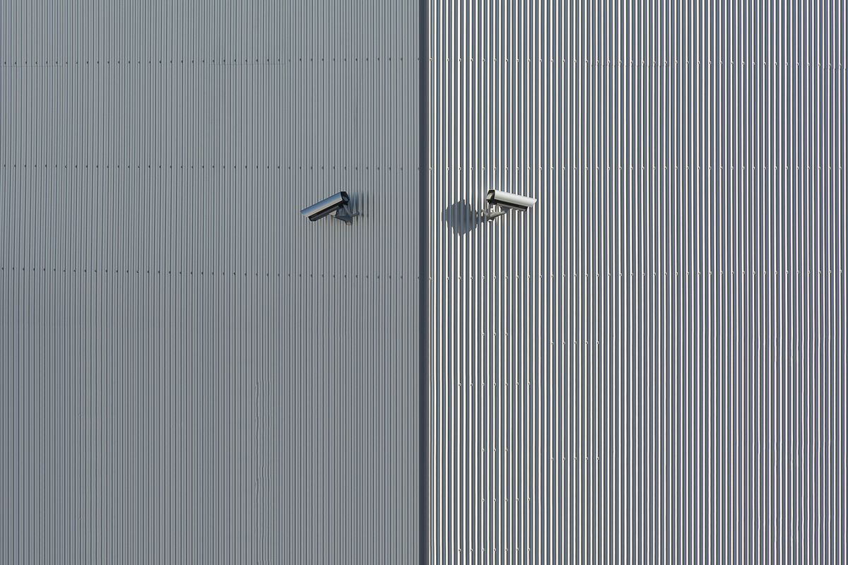 Two bullet security cameras on the corrugated metal wall of an industrial building