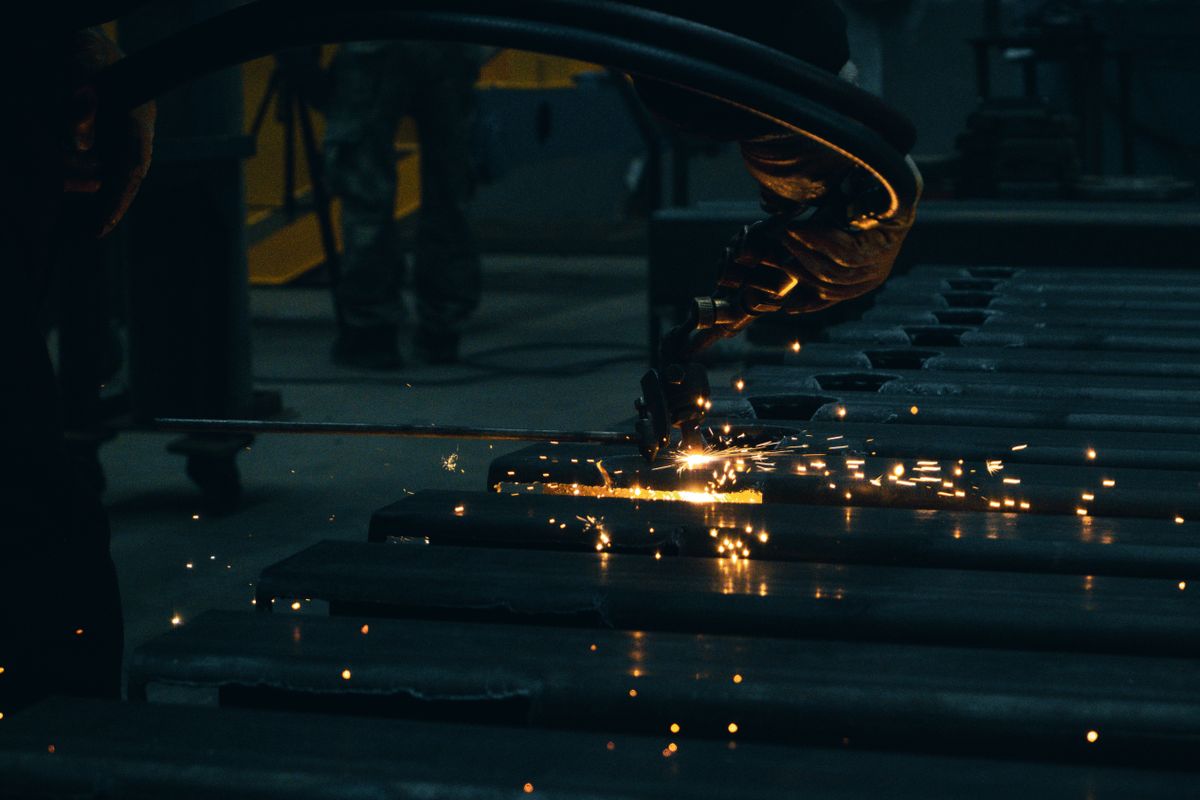 A worker torch-cutting steel plates on a fabrication shop floor, throwing sparks